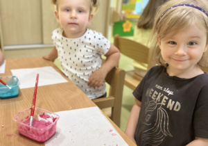 Dzieci zdobią ciastka na warsztatach cukierniczych. Na stole stoi różowy i niebieski lukier.