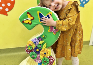 Blania trzyma styropianową cyfrę trzy, ozdobioną motylkami i kwiatkami