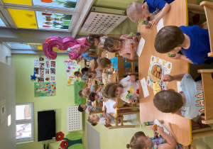 Dzieci siedzą przy stole i zajadają urodzinowy poczęstunek.