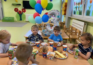 Dzieci siedzą przy stole i jedzą słodki poczęstunek.