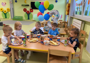 Dzieci siedzą przy stole i jedzą urodzinowy poczęstunek Oliwiera.