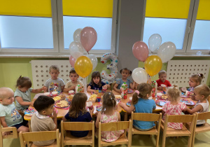 Dzieci siedzą przy stole i zajadają urodzinowy poczęstunek Poli.
