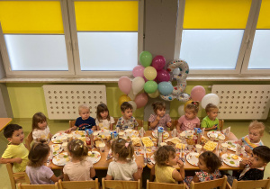 Dzieci siedzą przy stole i zajadają urodzinowy poczęstunek Helenki.