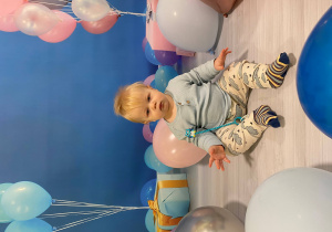 Jakub siedzi na dywanie i pozuje z balonami.
