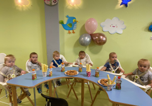 Dzieci siedzą przy stole i jedzą urodzinowy poczęstunek.