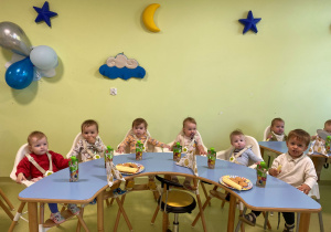Dzieci siedzą przy stole i jedzą urodzinowy poczęstunek Olafa.