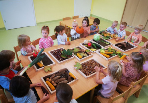 Dzieci siedzą przy stolikach, oglądają i manipulują darami jesieni.