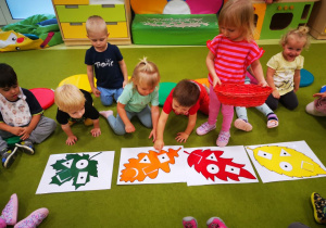 Dzieci dopasowują figury geometryczne z rzepami do dużych kolorowych liści ułożonych na dywanie.
