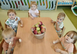 Dzieci siedzą przy stole i poznają smak jabłek.