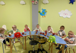 Dzieci siedzą przy stole i oglądają czerwone jabłuszka.
