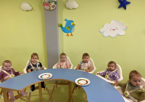 Dzieci siedzą przy stole i oglądają kolorową tęczę.