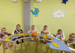 Dzieci siedzą przy stole i oglądają dary jesieni.