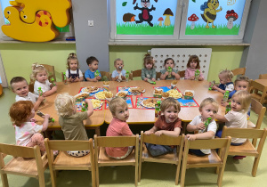 Dzieci siedzą przy drewnianym stoliku, na którym są położone smakołyki urodzinowe.