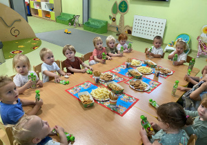 Dzieci siedzą przy drewnianym stoliku, na którym są położone urodzinowe słodkości.