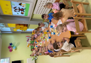 Dzieci siedzą przy drewnianym stoliku, na którym znajdują się słodkości.