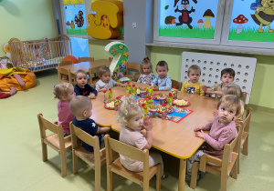 Dzieci siedzą przy drewnianym stoliku, na którym znajdują się urodzinowe słodkości.