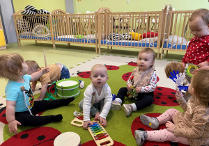 Dzieci siedzą na dywanie i grają na instrumentach muzycznych.