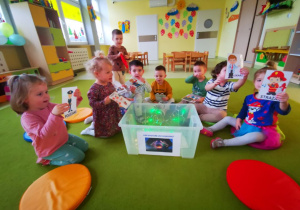 Dzieci siedzą na dywanie, uczestniczą w zabawie andrzejkowej.