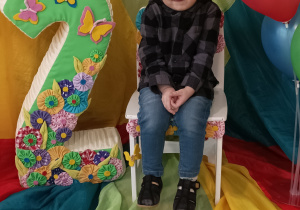 Olaf siedzi na urodzinowym krześle. Obok stoi cyfra dwa oraz kolorowe balony.