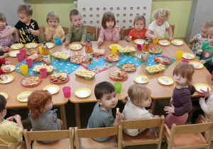 Dzieci siedzą przy stoliku i jedzą urodzinowe słodkości.