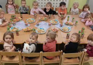 Dzieci siedzą przy stole i jedzą urodzinowe słodkości.