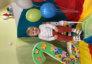 Julek siedzi na urodzinowym krześle. Obok niego stoi styropianowa cyfra dwa oraz kolorowe balony.