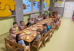 Dzieci siedzą przy stole i jedzą urodzinowe słodkości.