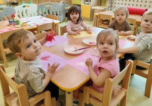 Dzieci siedzą przy stole i odbijają swoje dłonie w farbie.