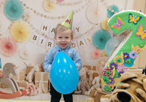 Józio z niebieskim balonem i cyfrą dwa pozuje do urodzinowego zdjęcia.