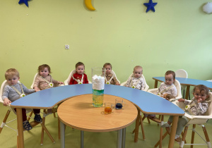 Dzieci siedzą przy stole i oglądają doświadczenie.