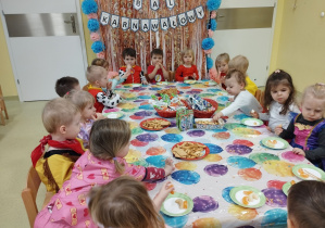 Dzieci siedzą przy stole i jedzą smakołyki.