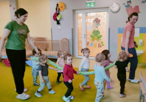 Dzieci wraz z opiekunkami trzymają węża do nauki wspólnego chodzenia.