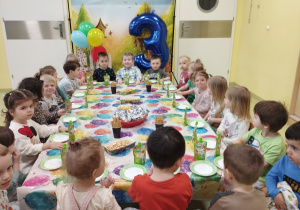 Dzieci siedzą przy stoliku i jedzą urodzinowe słodkości.