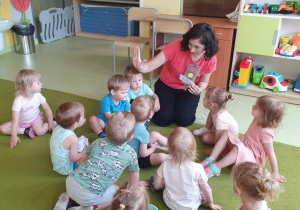 Dzieci siedzą na dywanie i poznają zasady bezpieczeństwa na drodze.