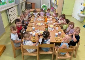 Dzieci siedzą przy stoliku i jedzą urodzinowe słodkości.