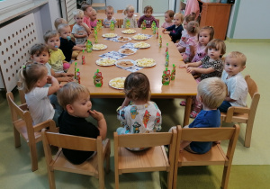 Dzieci siedzą przy stolikach i częstują się smakołykami urodzinowymi.