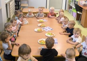 Dzieci siedzą przy stole i jedzą urodzinowe przekąski.