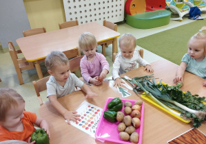 Dzieci siedzą przy stoliku i oglądają warzywa.