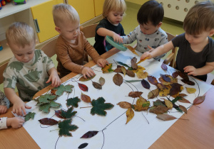 Dzieci siedzą przy stoliku i wyklejają wiewiórkę liśćmi.