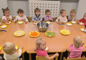 Dzieci siedzą przy stole. Na talerzykach stoją owoce z których będą wykonywały owocową sałatkę. Każde dziecko ma swój talerzyk oraz plastikowy nóż.