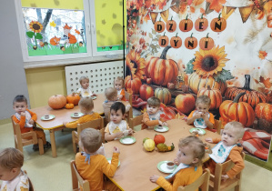 Dzieci siedzą przy stolikach i jedzą dyniowe babeczki.