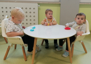 Nicolas, Hania, Roksana siedzą przy stoliku i ugniatają plastelinę.