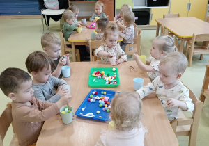 Dzieci siedzą przy stoliku i bawią się pomponami.