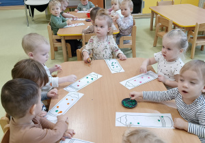 Dzieci siedzą przy stoliku i wyklejają kredkę plasteliną.