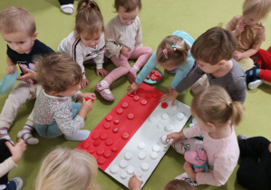 Dzieci układają korki białe i czerwone na dużej fladze Polski.