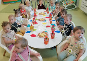 Dzieci siedzą przy stolikach i jedzą ciasteczka.