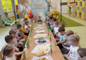 Dzieci siedzą przy stole i jedzą smakołyki.