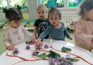 Hania, Mark i Roksana przyklejają kwiaty bzu na kartce papieru..