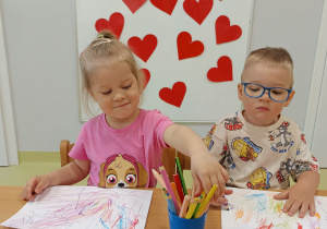 Karolina i Wojtek kolorują kartkę na kolorowo, aby przygotować laurki.