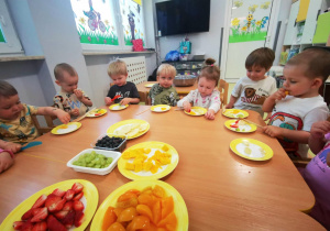 Dzieci siedząc przy stolikach kroją składniki na sałatkę owocową.